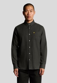 Camisa de manga larga verde oscuro de algodón, con cuello abotonado, bolsillo delantero y un pequeño logotipo amarillo en el pecho.
