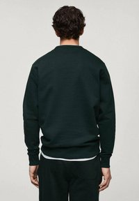 Ciemnozielona bluza z okrągłym dekoltem i prążkowanymi mankietami. Miękka, teksturowana tkanina, o luźnym kroju. Brak widocznych logo i ozdobników.