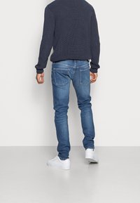 Smalblå denimjeans med fem fickor, ljus tvätt och en klassisk design. Matchas med en mörk, strukturerad stickad tröja och vita sneakers.