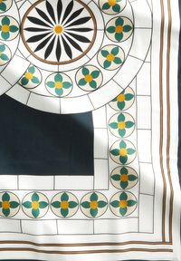Foulard en soie carré avec un motif floral décoratif en teal et jaune, agrémenté de formes géométriques noires et blanches.