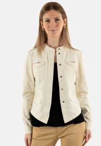 Giacca in denim color crema con colletto alto, chiusura anteriore a bottoni, due tasche sul petto e sottili dettagli ricamati lungo la spalla.