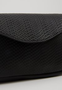 Pochette noire texturée présentant un motif en peau de serpent avec une finition lisse et une fermeture à rabat, mettant en avant un design épuré et une esthétique moderne.