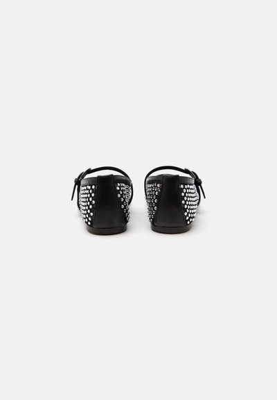 Paire de chaussures plates noires avec des brides à la cheville, décorées de multiples petits clous brillants, vues de dos sur fond blanc.