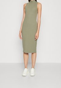 Robe midi côtelée vert olive avec un col haut et un design sans manches, assortie à des baskets blanches. Texture lisse, silhouette ajustée.