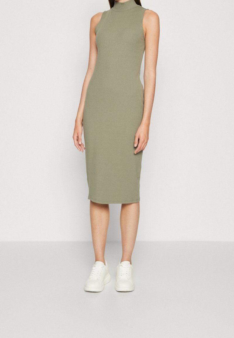 Robe midi côtelée vert olive avec un col haut et un design sans manches, assortie à des baskets blanches. Texture lisse, silhouette ajustée.
