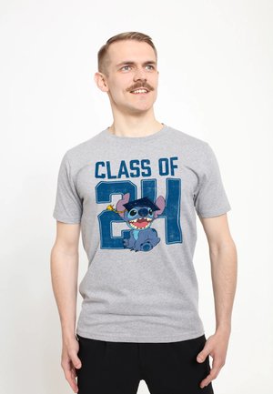 Mężczyzna z wąsami w szarej koszulce "Class of 21" z uśmiechniętą niebieską postacią z kreskówki w czapce absolwenta.