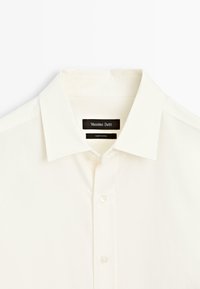 Camicia bianca con bottoni di Massimo Dutti. Tessuto morbido, colletto a punta e cuciture sottili. Presenta un'etichetta nera con il nome del marchio.