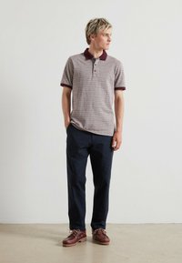 Polo shirt met korte mouwen in gestructureerd lichtbruin met maroon kraag, gecombineerd met marineblauwe broek en bruine bootschoenen met een witte zool.
