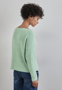 Suéter verde menta hecho de material esponjoso, con un escote amplio y mangas largas, combinado con jeans de mezclilla azul.