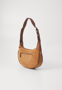 Sac en suède marron avec une forme courbe, des accents en cuir et une poche zippée dorée à l'avant. Il dispose d'une bandoulière réglable.