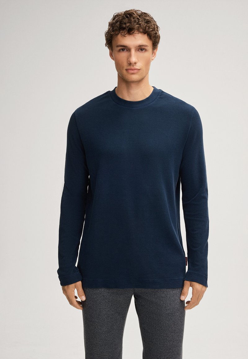 Marineblaues Langarm-T-Shirt aus strukturiertem Stoff mit Rundhalsausschnitt. Verfügt über minimale Nähte und seitliche Schlitze, getragen mit karierten Hosen.