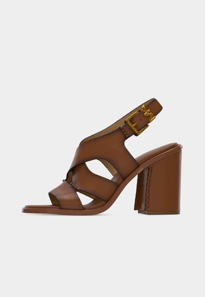 Brun lær høyhælte sandal med brede stropper, åpen tå, slingback-design og gullfarget spenne på tykk blokkhæl.