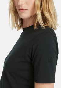 Černé tričko s krátkým rukávem vyrobené z bavlny, s kulatým výstřihem a texturovaným logem na levém rukávu. Hladký, přiléhavý design.