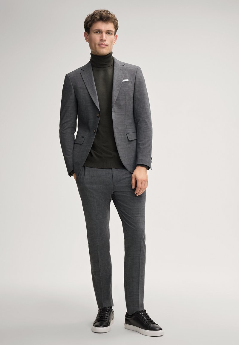 Grau karierter Anzug mit einem einreihigen Sakko, einem dunkelgrünen Rollkragenpullover und schwarzen Sneakers. Glatter Stoff mit modernem Schnitt.