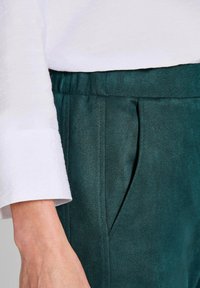 Teal, zacht-gebreide broek met plooien, voorzien van een tailleband en zijzakken, gecombineerd met een wit langärmige top.