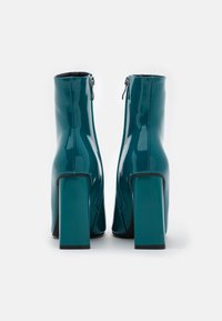 Botines de charol en color aguamarina con tacón cuadrado, cierre de cremallera lateral y textura suave. Terminados con suelas de goma negra.