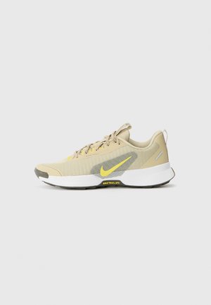 Hardloopschoenen van beige mesh met gele accenten. Beschikt over een grijs textuurpaneel, een dikke witte zool en een zwart rubberen profiel voor grip.