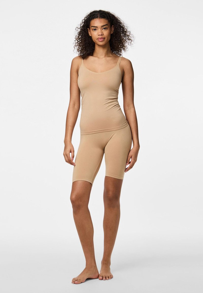 Bež brezšivna majica z tankimi naramnicami in ujemajoče srednje dolgimi kratkimi hlačami, obe izdelani iz gladkega, raztegljivega materiala.