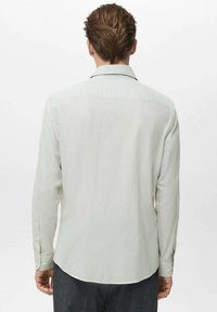 Camisa de manga larga a rayas verde claro con cuello, puños abotonados y dobladillo curvado. El material parece suave con una textura sutil.
