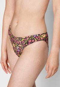 Parte de baixo de biquíni floral com um fundo preto, apresentando flores vibrantes em rosa, roxo e verde. Tecido suave e design de cintura baixa.