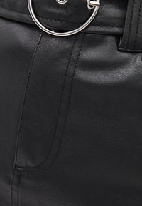 Černá kabelka z umělé kůže s kulatým kovovým kroužkem, hladkým povrchem a viditelným prošíváním po stranách.