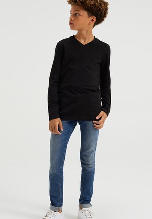 Chemise noire à manches longues en V associée à un jean slim bleu et des baskets blanches ; texture lisse, design simple et sans motifs visibles.