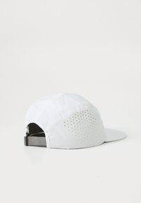 White baseball cap with a curved brim, made from lightweight material, featuring a ventilated panel with small perforations on one side.
