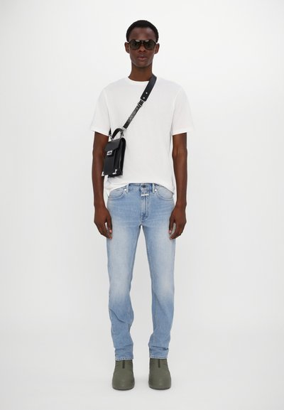 Black crossbody bag with silver hardware, white t-shirt, light blue jeans, and green ankle boots. Model wearing dark sunglasses.