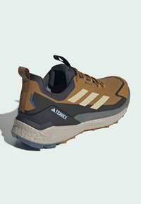 Brązowy i czarny but sportowy z materiału Gore-Tex, teksturowanym wierzchem, trzema białymi paskami oraz wyrazistym logo TERREX po boku.