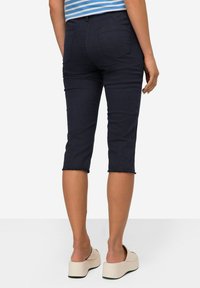 Pantalons capri en denim bleu marine avec ourlet effiloché, dotés de deux poches arrière et d'une coupe slim, accompagnés de sandales à plateforme de couleur claire.