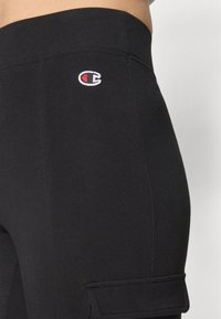 Svarta träningsleggings i stretchigt tyg, med ett broderat logotyp och en sidficka. Slät textur och åtsittande design.