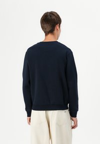 Sweatshirt col rond bleu marine avec des poignets et un ourlet côtelés, fabriqué à partir d'un tissu doux, avec une coupe décontractée. Étiquette logo visible sur le côté inférieur.