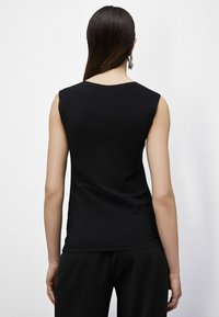 Top nero senza maniche con una silhouette aderente, texture liscia e scollatura rotonda, abbinato a pantaloni neri ampi.