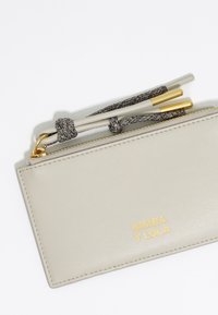 Portafoglio in pelle grigio chiaro con chiusura a zip, dotato di una fascia in tessuto texturizzato e accessori in metallo dorato. Logo stampato in oro sulla parte anteriore.