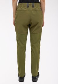 Oliv green turistické kalhoty s elastickým pasem, plochými švy a zesílenými kolenními oblastmi. Materiál vypadá lehký a odolný.