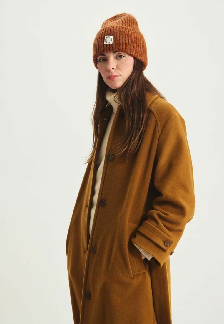 Manteau en laine mélangée marron à coupe décontractée, doté de grands boutons et de poches latérales. Associé à un bonnet côtelé orange et un pull léger.