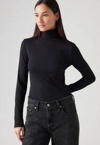 Haut à col roulé noir côtelé avec des manches longues, associé à un jean foncé taille haute. La texture est lisse et ajustée.