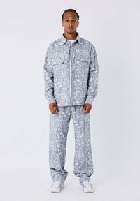 Lichtblauwe, gestreepte outfit met een knoopjasje met twee voorzakken en loszittende broeken. Gemaakt van een zachte stof met een tropisch ontwerp.