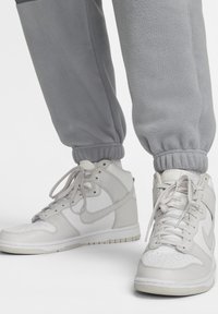 Pantalones de sudadera de felpa gris con tobillos fruncidos, combinados con zapatillas deportivas altas blancas que tienen detalles y cordones en gris claro.