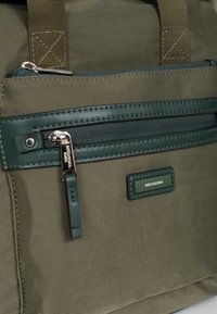 Borsa in nylon verde oliva con tessuto testurizzato, dotata di tasca anteriore con zip, dettagli in pelle verde e etichetta del marchio. Manici rinforzati.