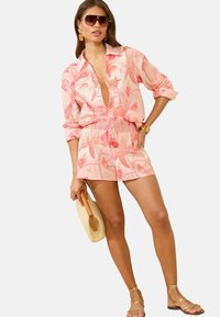 Light pink outfit with a deep V-neck shirt featuring shell patterns and matching shorts, smocked waistband, and beige accessories.
