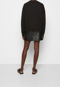 Sudadera negra de corte oversize con hombros caídos, combinada con una falda de cuero negra ajustada. Modelo que lleva sandalias negras planas.