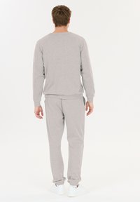 Grauer Baumwoll-Sweatshirt und passende Jogginghose. Gerippte Bündchen und Taillenausschnitt. Glatte Textur, lockere Passform. Weiße Sneaker runden das Outfit ab.