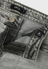 Jeans in denim grigio con chiusura a zip e bottone. Texture lavata e dettagli di cucitura notevoli, con etichetta che indica la taglia 14S.
