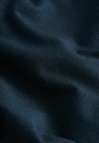 Tmavomodrý textil s hladkým, textúrovaným povrchom, s jemnými ryhami a mäkkým padaním. Jemné záhyby vytvárajú dynamický vzhľad.