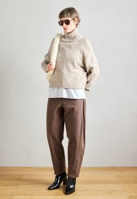 Béžový pletený rolák, pod ním světle modrá košile, hnědé volné kalhoty a černé kozačky na podpatku.