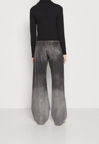 Svart långärmad topp i kombination med vida jeans i en gråskala, med en urblekt struktur och kontrasterande sömnadsdetaljer.