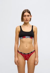 Brassière de sport noire avec une large bande logo et bas de bikini rouge avec un motif de cannes en sucre d'orge, les deux en tissu lisse.
