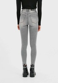 Vysoko pasové šedé džíny s úzkým střihem, s dvěma zadními kapsami a vybledlou texturou, doplněné černými platformovými botami.