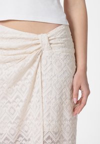 Crème geborduurde rok met diamanten en bloemmotieven, gestructureerde stof, ruching aan de zijkant en een gefalte tailleband.